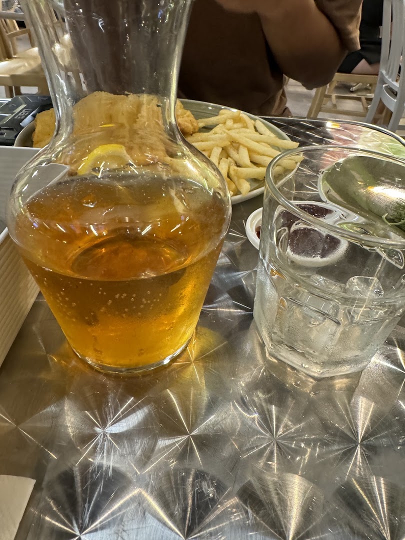 A refreshing carafe of iced tea and a glass of water on a metallic table, with fries in the background.