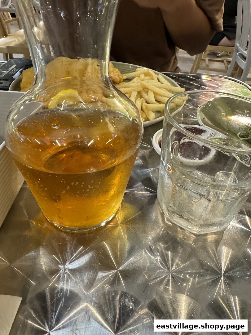 A refreshing carafe of iced tea and a glass of water on a metallic table, with fries in the background.