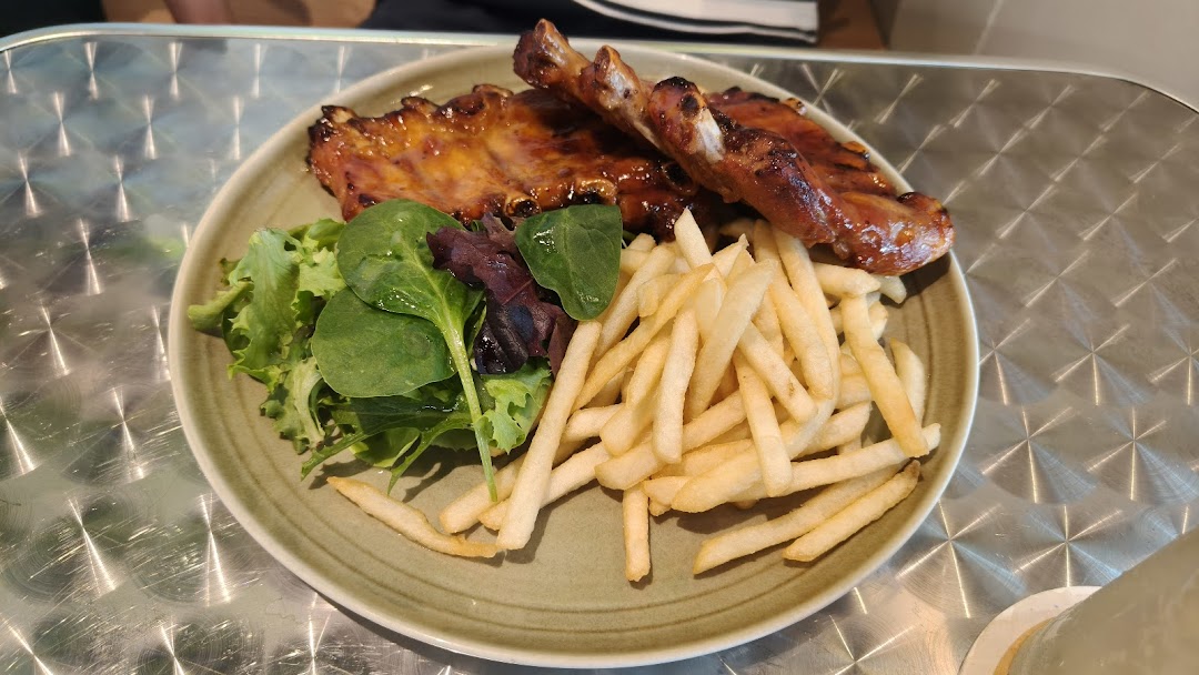 A plate of glazed ribs, golden fries, and fresh green salad on a textured metal table.