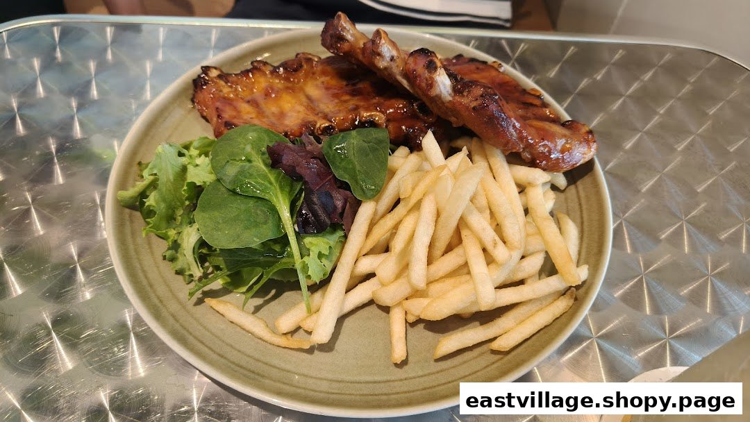 A plate of glazed ribs, golden fries, and fresh green salad on a textured metal table.
