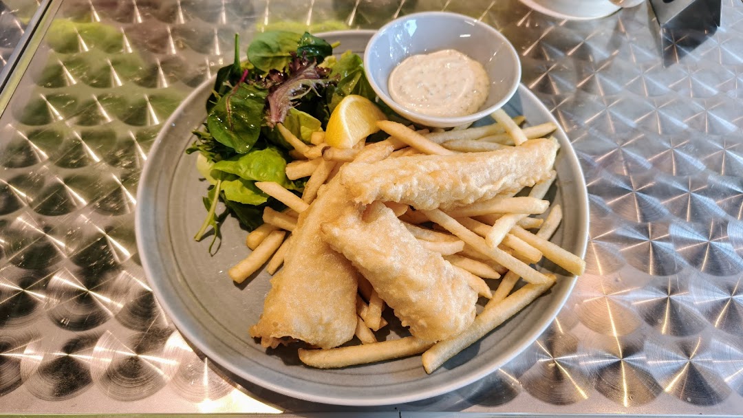 A plate of golden-fried fish and chips with a side salad, lemon wedge, and dipping sauce.