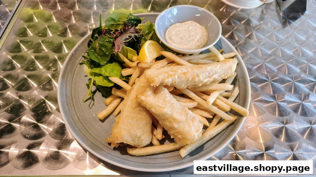 A plate of golden-fried fish and chips with a side salad, lemon wedge, and dipping sauce.