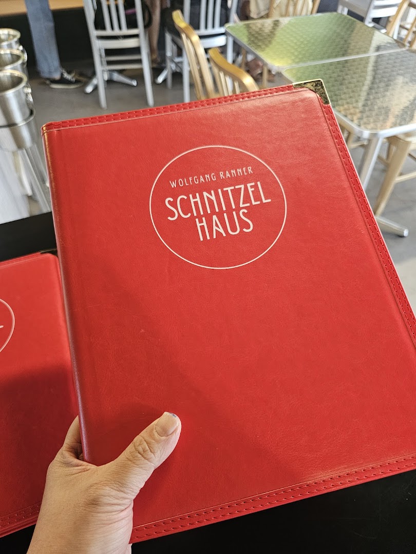 A hand holds a red menu cover for Schnitzel Haus Wolfgang Ranner inside the restaurant.