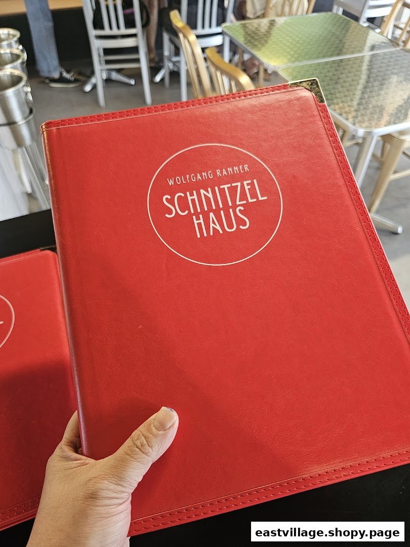 A hand holds a red menu cover for Schnitzel Haus Wolfgang Ranner inside the restaurant.