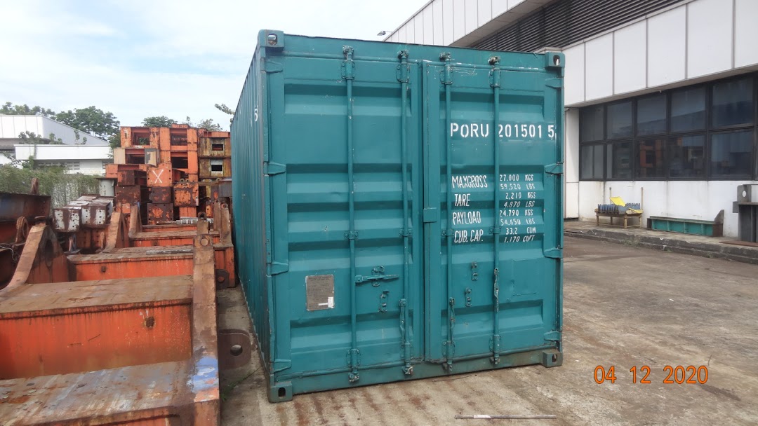A large green shipping container stands amidst industrial equipment and structures in an outdoor yard.