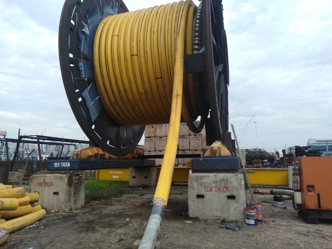 A large industrial reel with yellow piping in an outdoor industrial yard setting.