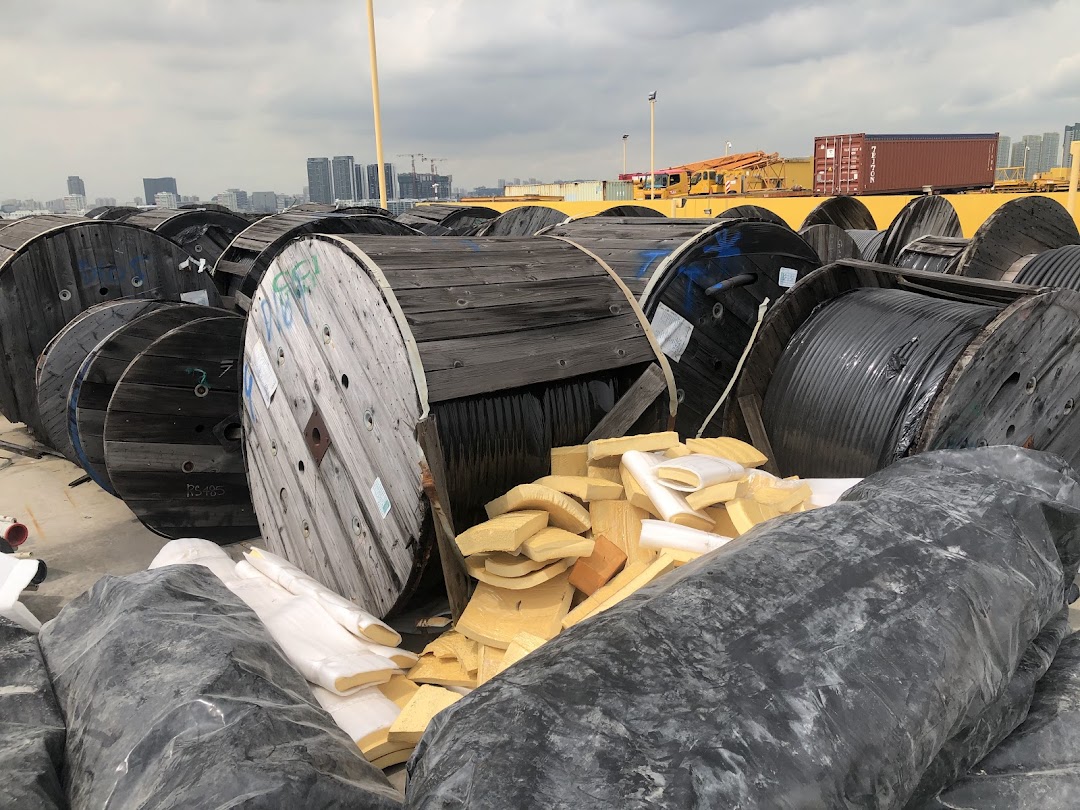 Large industrial cable spools and materials stored outdoors with a city skyline in the background.