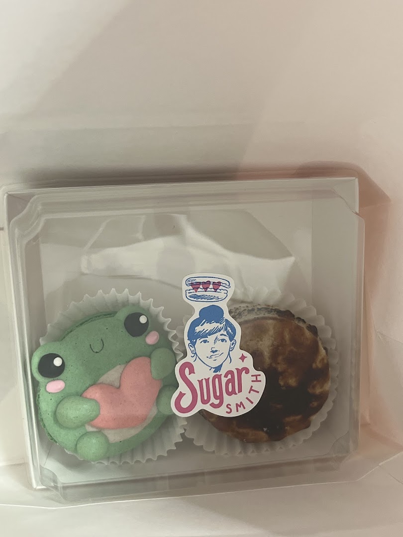 Two delightful pastries, including a frog-shaped macaron, in a clear box from Sugarsmith.