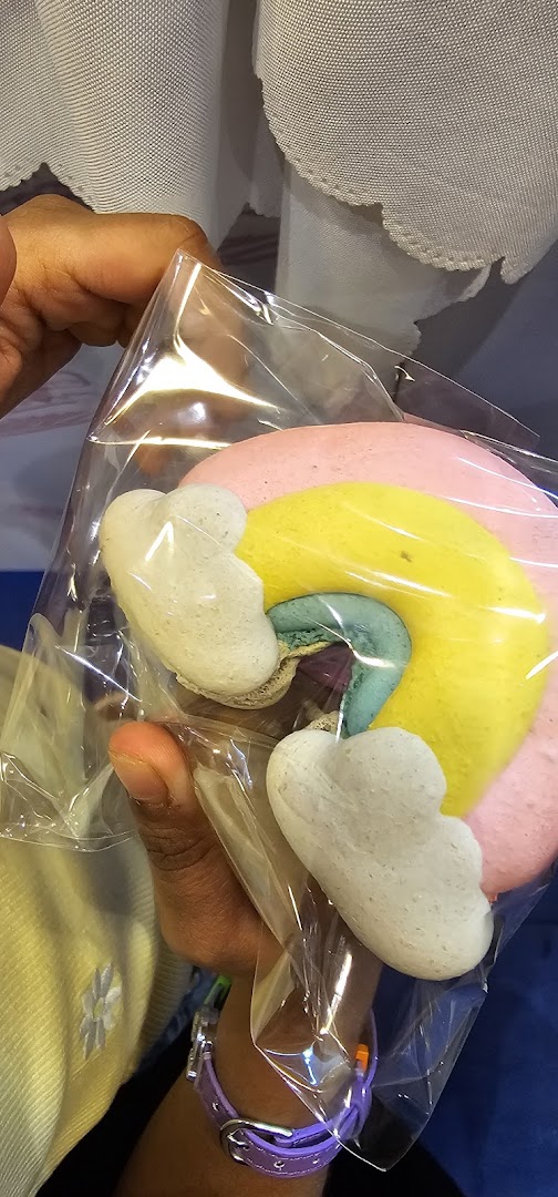 A hand holds a clear bag containing colorful, whimsical cloud and rainbow-shaped meringue cookies or macarons.