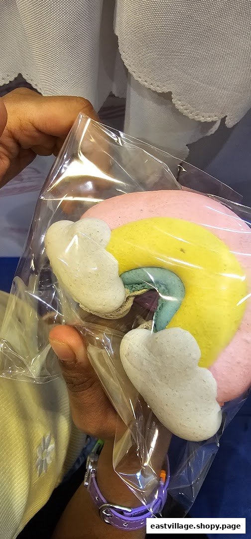 A hand holds a clear bag containing colorful, whimsical cloud and rainbow-shaped meringue cookies or macarons.