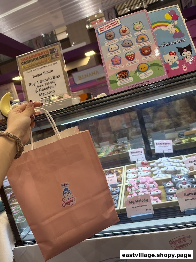 A hand holds a Sugarsmith shopping bag in front of a display case filled with adorable character macarons and promotional signs.