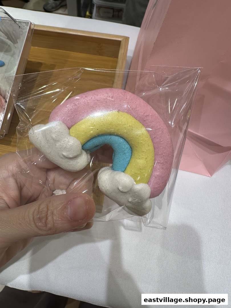 A hand holds a colorful rainbow-shaped sweet treat, likely a macaron, from Sugarsmith.