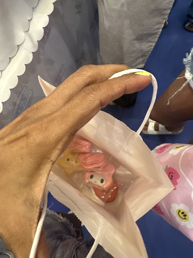 A hand holds a white paper bag containing character-themed macarons from Sugarsmith.