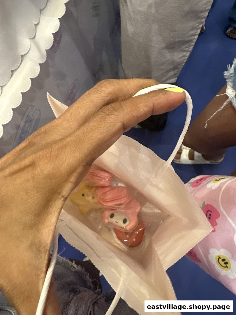 A hand holds a white paper bag containing character-themed macarons from Sugarsmith.