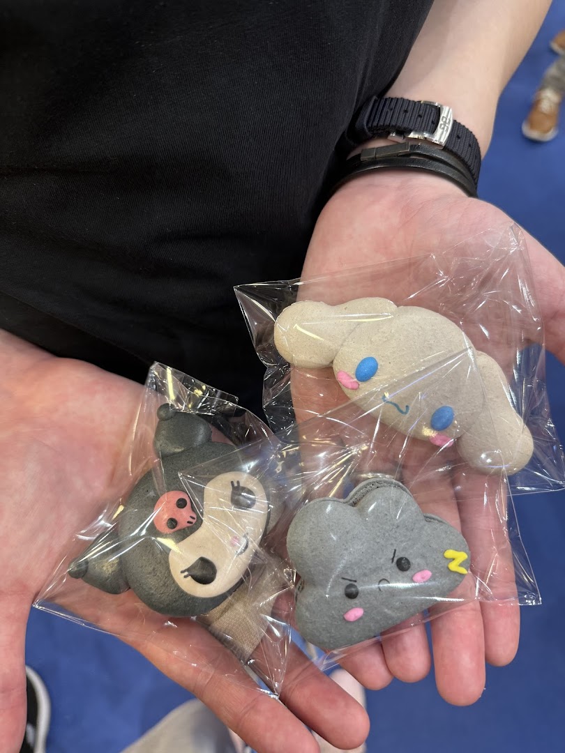Hands holding three individually wrapped, character-shaped sweet treats from Sugarsmith, featuring cute designs.