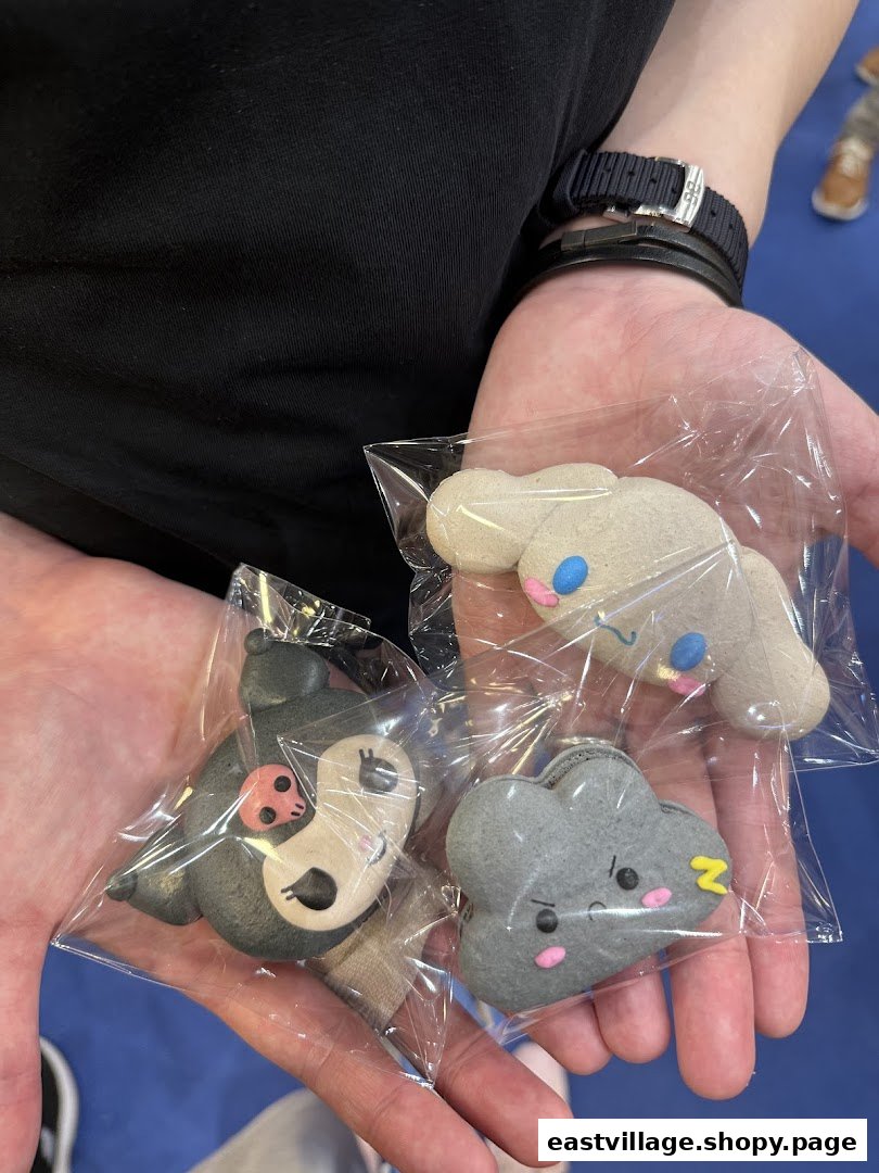 Hands holding three individually wrapped, character-shaped sweet treats from Sugarsmith, featuring cute designs.