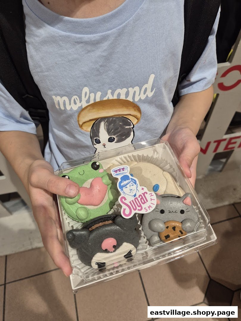 A person holds a clear box of adorable character macarons from Sugarsmith, featuring various cute designs.