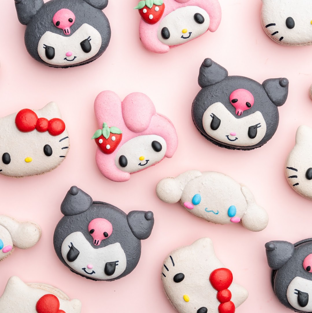 A vibrant collection of character-themed macarons, including Hello Kitty, My Melody, Kuromi, and Cinnamoroll, on a pink background.