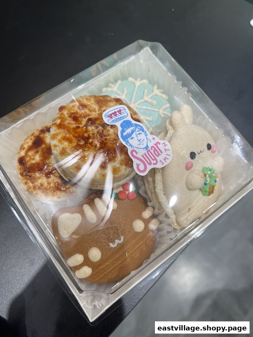 A clear box filled with assorted festive and whimsical baked goods from Sugarsmith, including cookies and tarts.