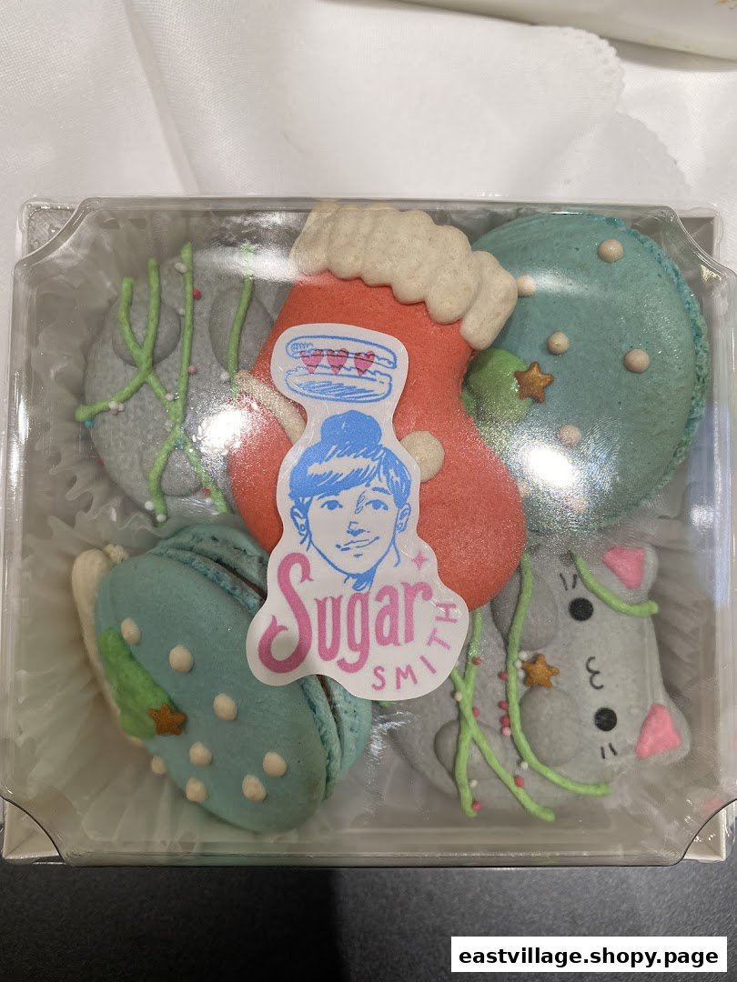 A clear plastic box filled with festive, holiday-themed macarons from Sugarsmith, featuring various shapes and decorations.
