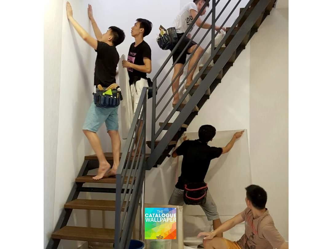 Skilled team members from The Catalogue Wallpaper installing wallpaper on a wall next to a modern staircase.