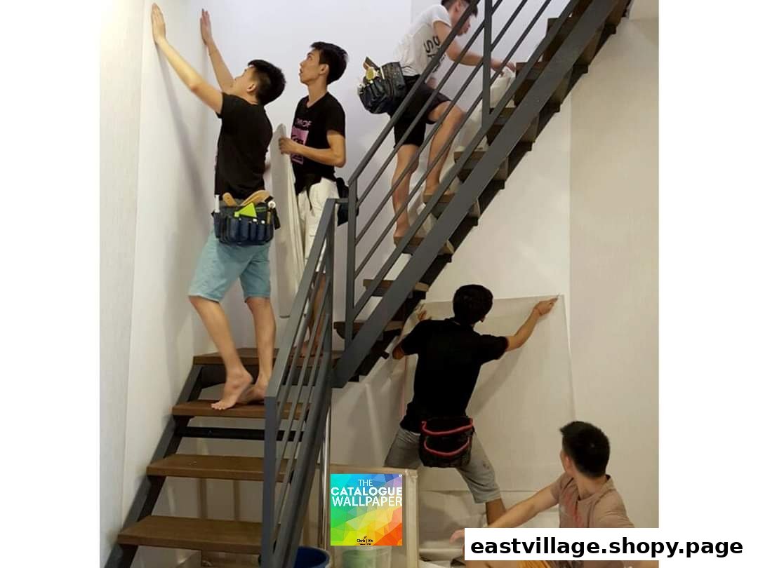 Skilled team members from The Catalogue Wallpaper installing wallpaper on a wall next to a modern staircase.