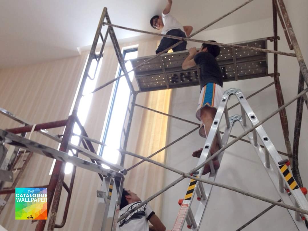 Workers on scaffolding and ladders installing wallpaper or working on a ceiling in a room.