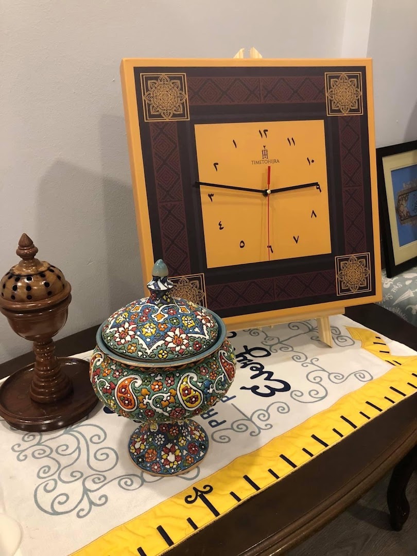 A decorative clock with Arabic numerals, a colorful ceramic pot, and a wooden incense burner on a table.