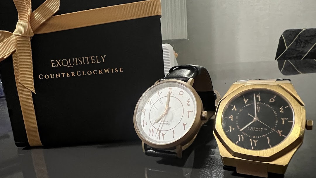 Two unique watches with Arabic numerals displayed alongside a gift box from 'Time To Hijra'.