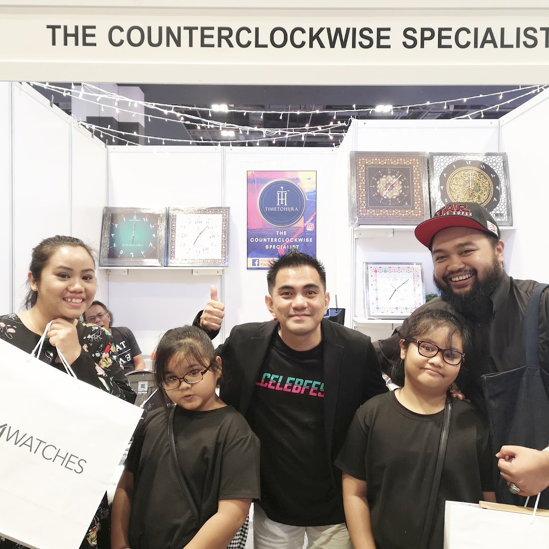A group of people smiling in front of the 'Time To Hijra' booth, showcasing unique counter-clockwise clocks.