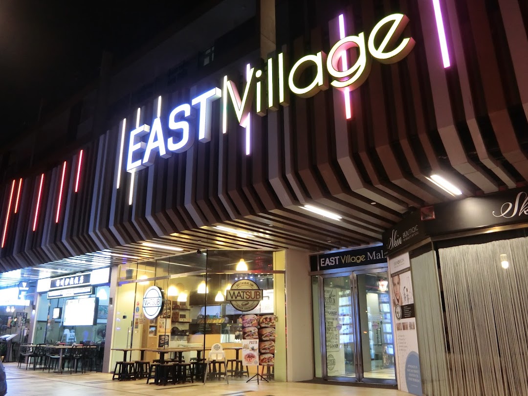Illuminated entrance of East Village mall at night, featuring various shop fronts including WATSUB.