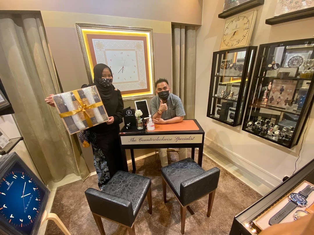 Two masked individuals, likely staff, inside a watch and clock shop with display cases and a gift.
