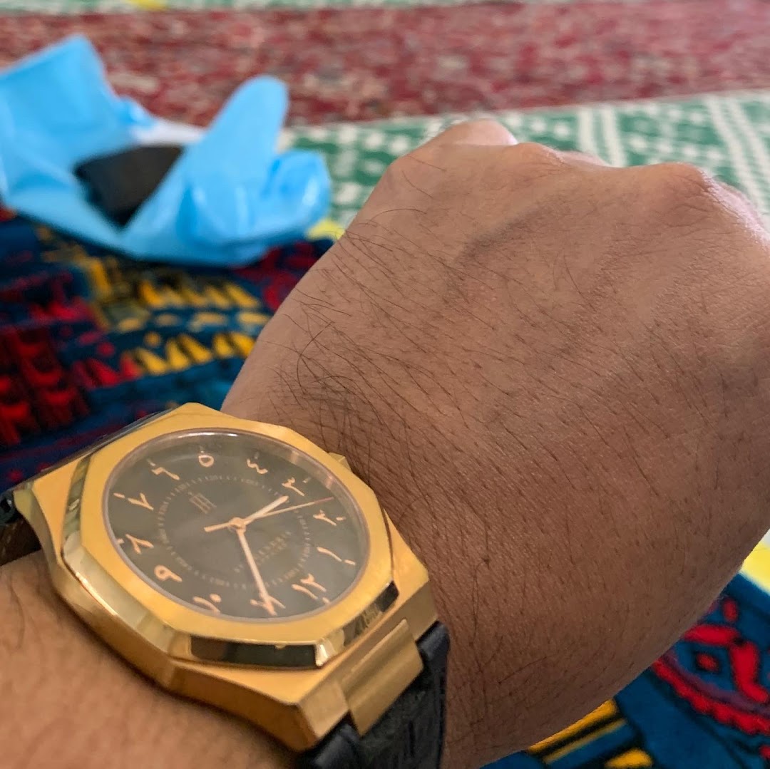 A close-up of a person's arm wearing an elegant gold watch with Arabic numerals on a patterned background.