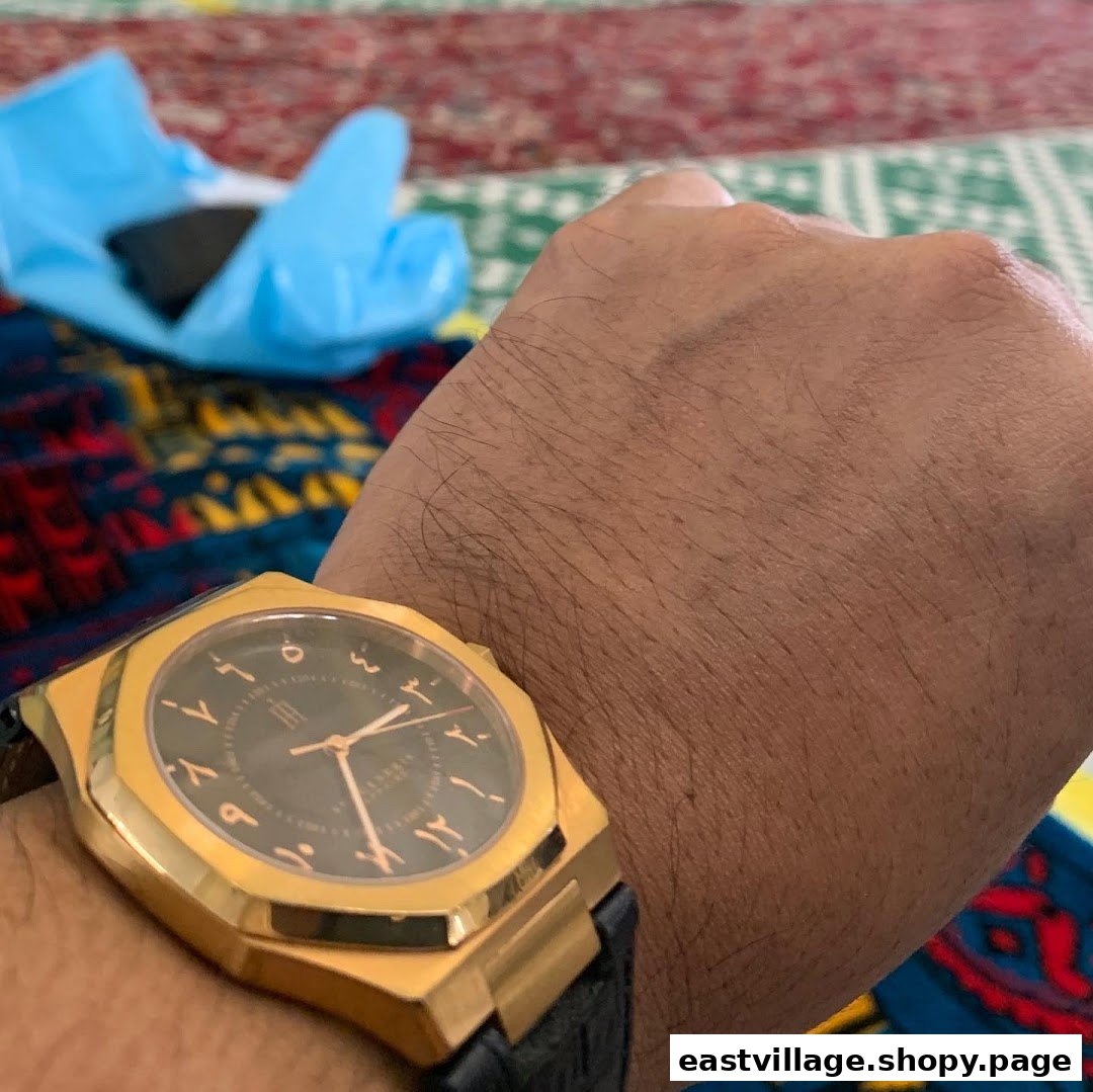 A close-up of a person's arm wearing an elegant gold watch with Arabic numerals on a patterned background.