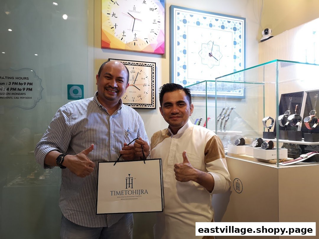 Two smiling men pose with a shopping bag inside Time To Hijra, a watch and clock shop.