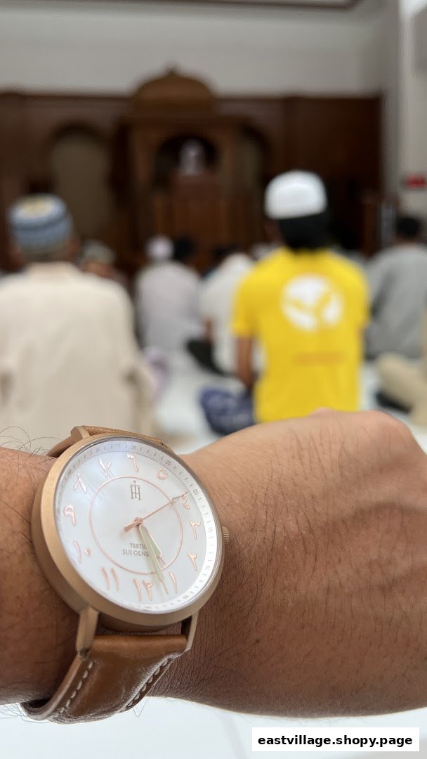 A close-up of a watch with Arabic numerals on a wrist, with blurred figures praying in the background.