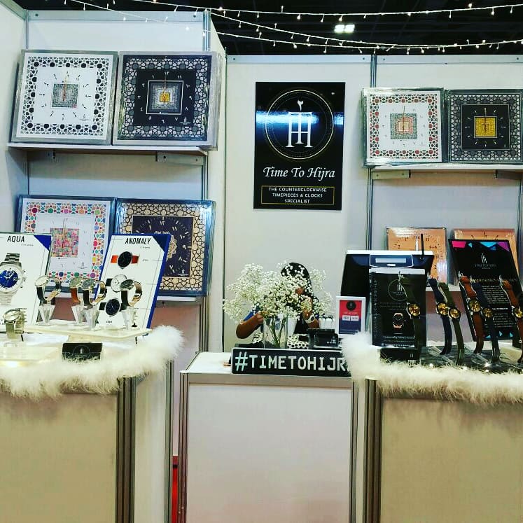 A retail booth for 'Time To Hijra,' showcasing unique counter-clockwise timepieces and decorative clocks.