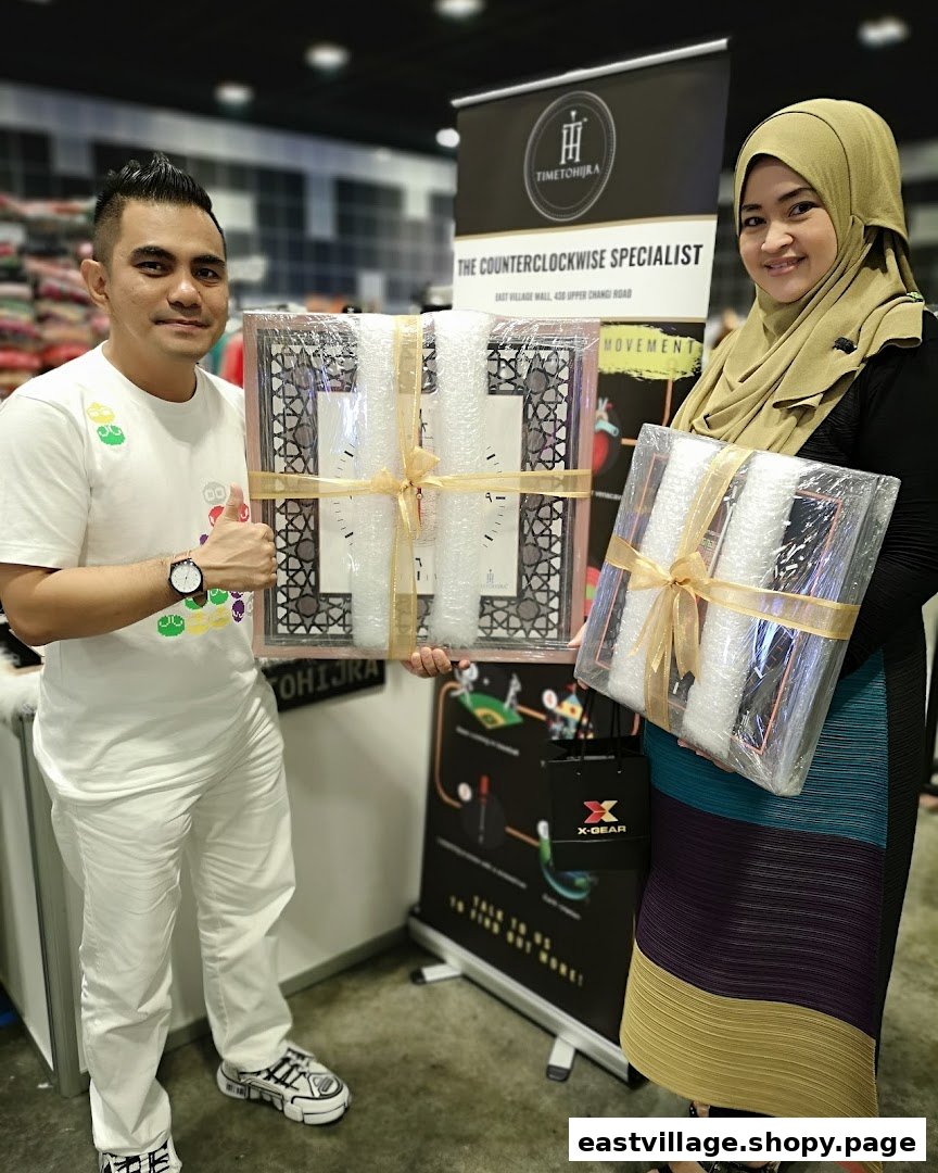 Two individuals proudly display packaged counterclockwise clocks from 'Time To Hijra' at their booth.