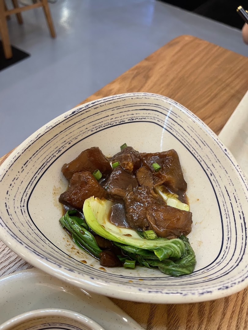 A close-up of a delicious braised meat dish with green vegetables served in a patterned bowl.