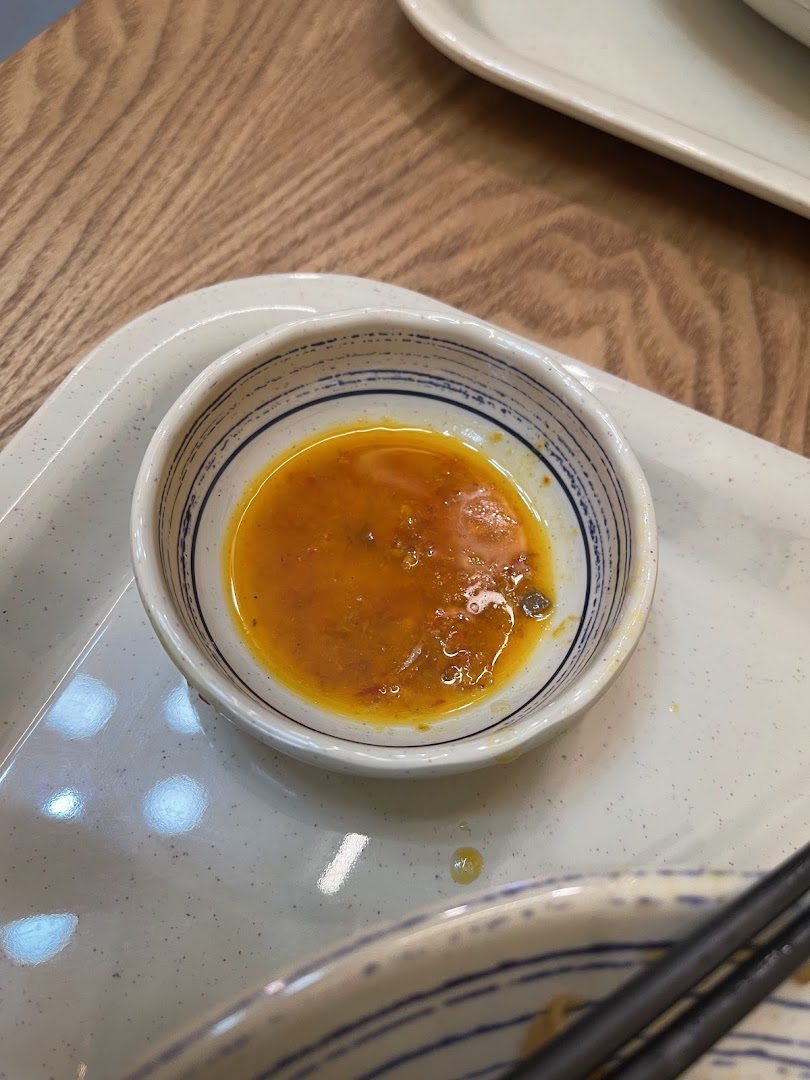 A close-up of a small bowl of vibrant orange chili sauce on a speckled tray, ready for dipping.