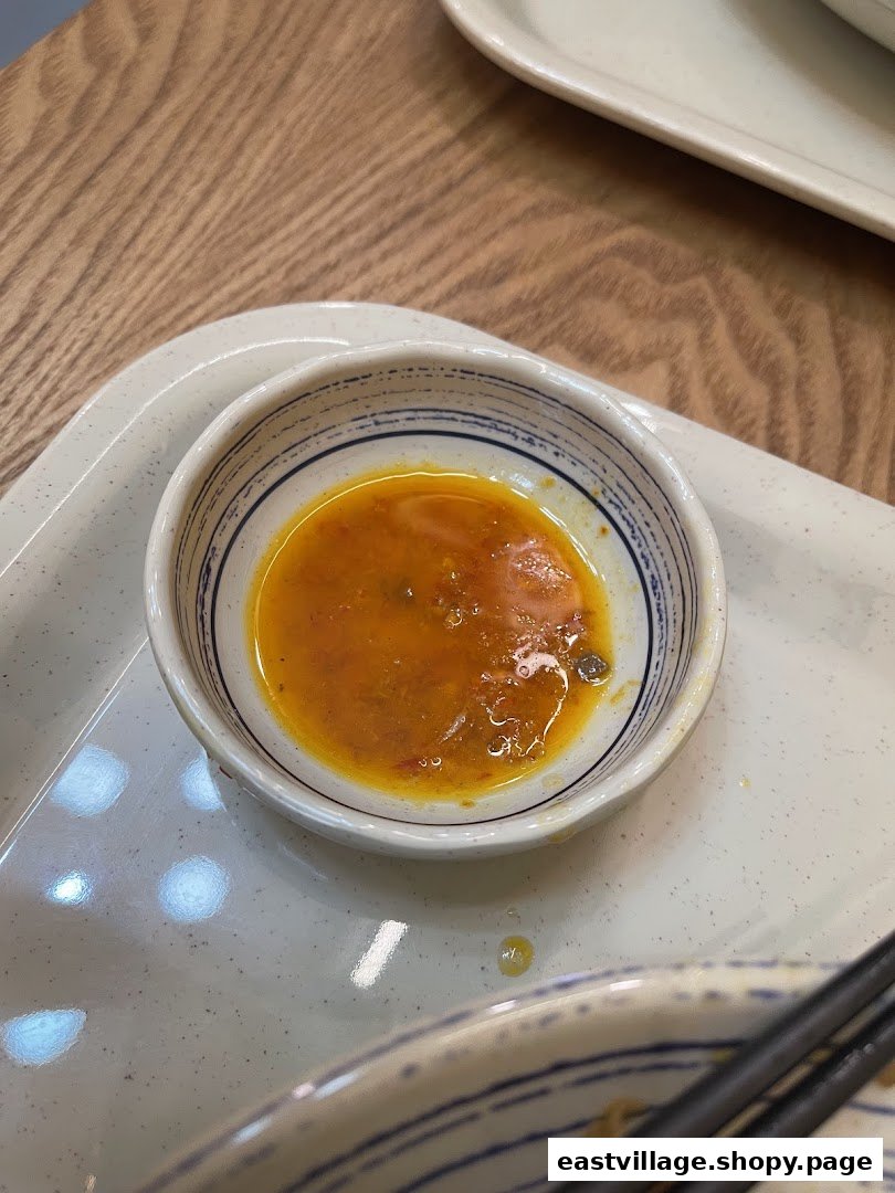 A close-up of a small bowl of vibrant orange chili sauce on a speckled tray, ready for dipping.