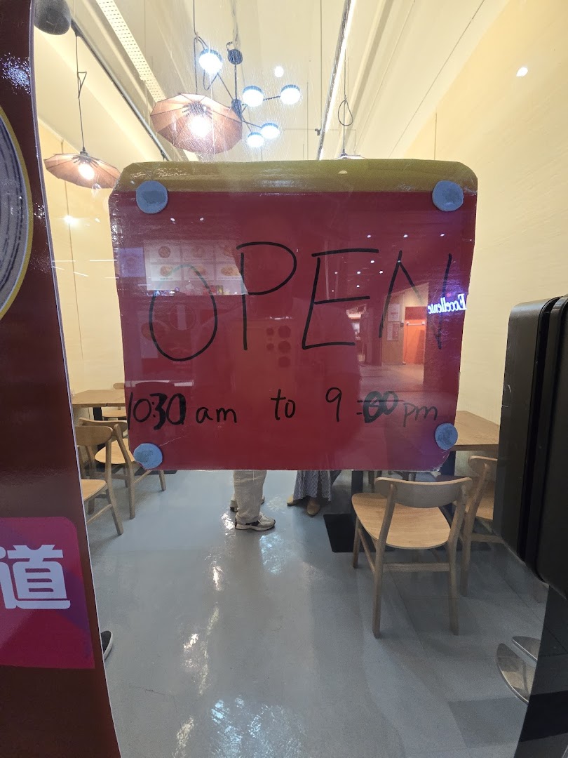 A clear view of the shop's glass entrance displaying an 'OPEN' sign and daily operating hours.