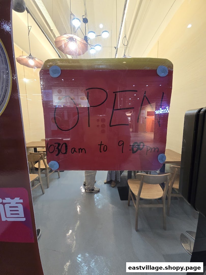 A clear view of the shop's glass entrance displaying an 'OPEN' sign and daily operating hours.