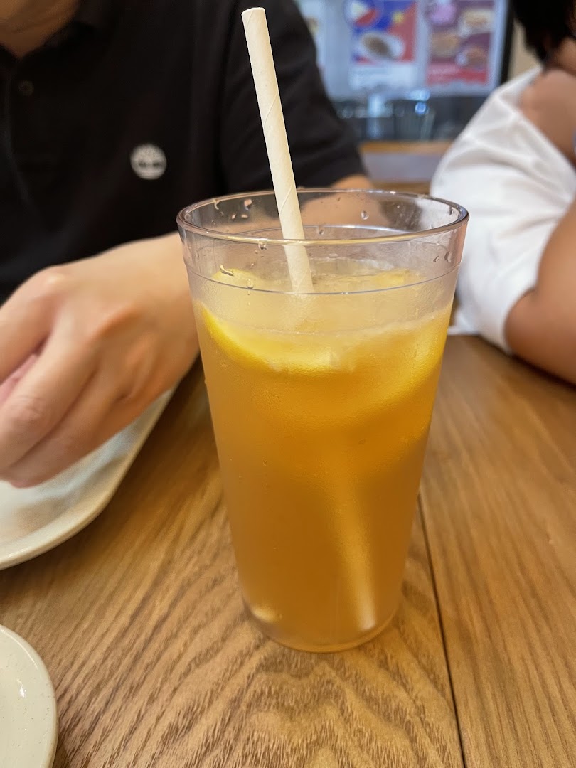 A refreshing glass of iced lemon tea with lemon slices and a paper straw on a wooden table.