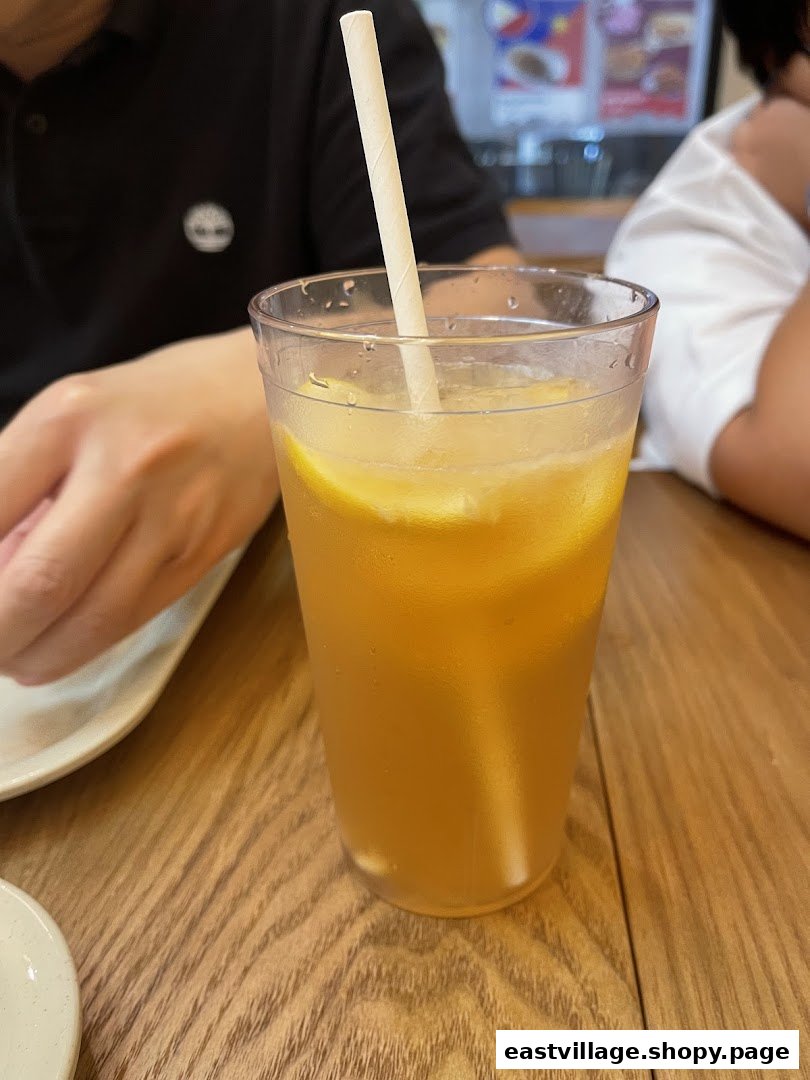A refreshing glass of iced lemon tea with lemon slices and a paper straw on a wooden table.