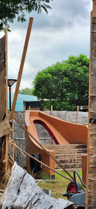 A playground slide is seen through construction materials and wooden supports.
