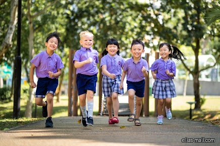 Five children in uniforms are running and smiling on a path.