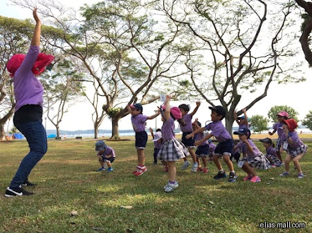 Children and a teacher are exercising outdoors on a grassy field.