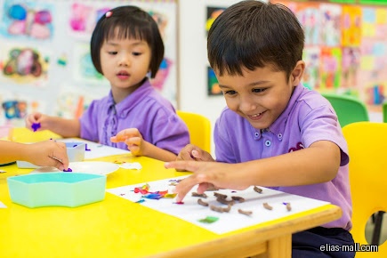 Children in purple shirts are doing crafts at a yellow table.
