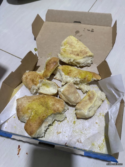 An open Domino's pizza box contains leftover bread pieces with yellow seasoning.